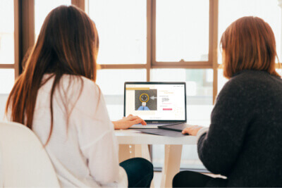 two women sitting at a table and looking at a website created by Joy Street Web Design